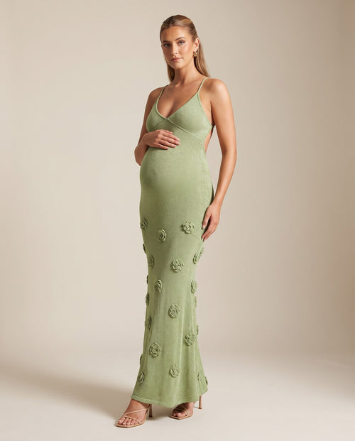 Sage green shimmer knit maternity maxi dress with 3D flowers, cami straps and open tie back, shown on a pregnant model in studio.