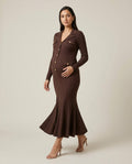 Brown ribbed knit maternity maxi dress with collar, gold buttons and fluted hem, shown on a pregnant model in studio.