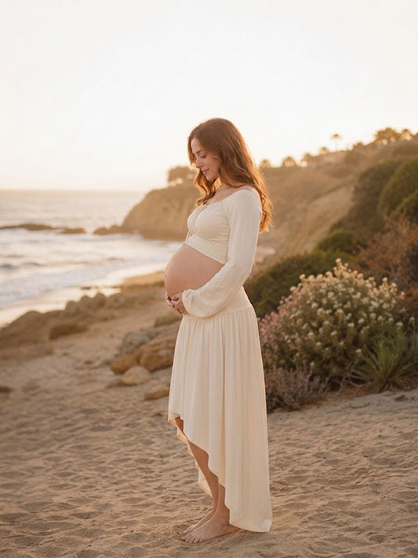 Side view of ivory maternity two-piece set with bell sleeve crop top and high-low skirt, designed for beach photoshoot.