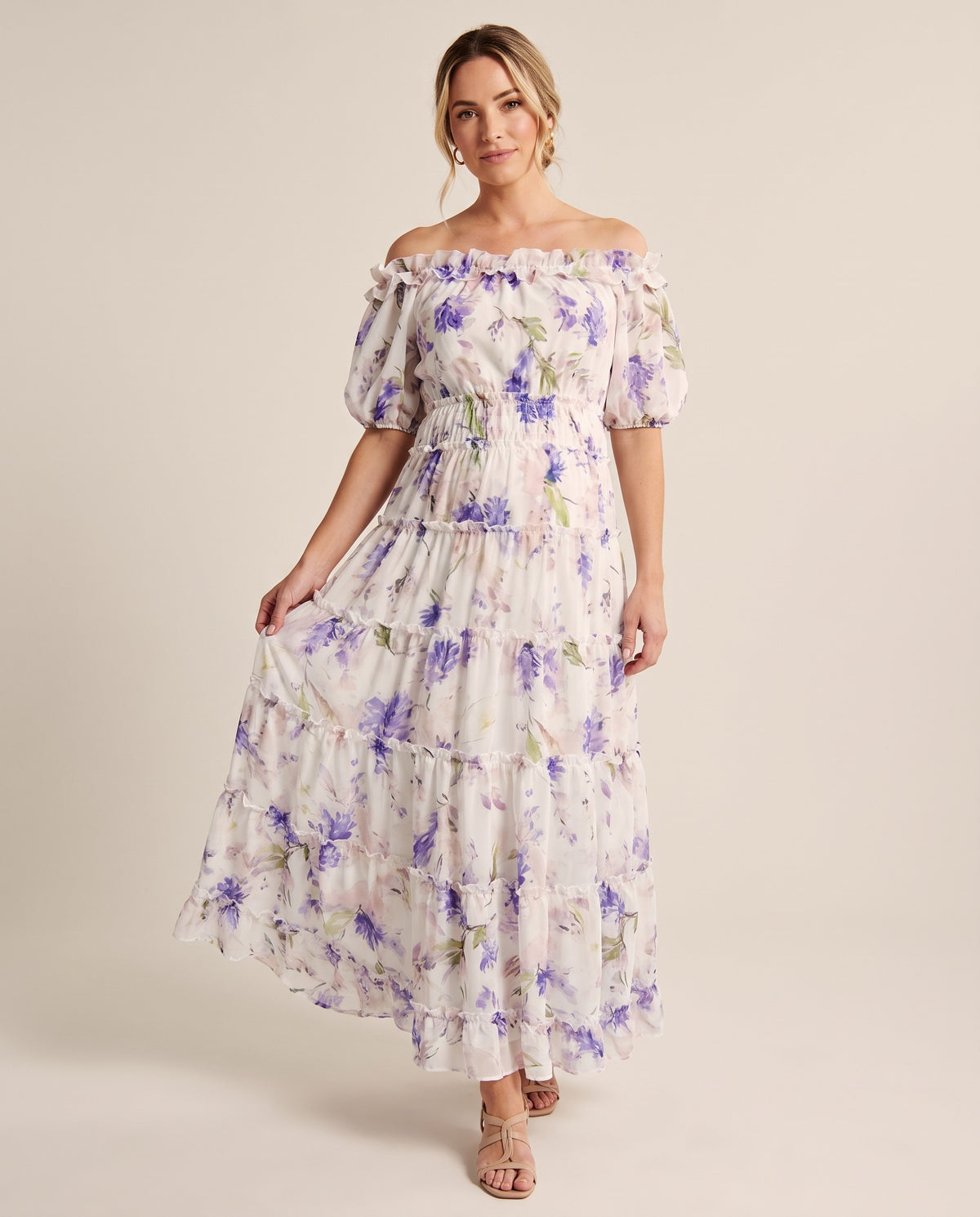 White floral print chiffon maternity maxi dress with off-shoulder neckline, puff sleeves and tiered skirt, shown on a pregnant model in studio.