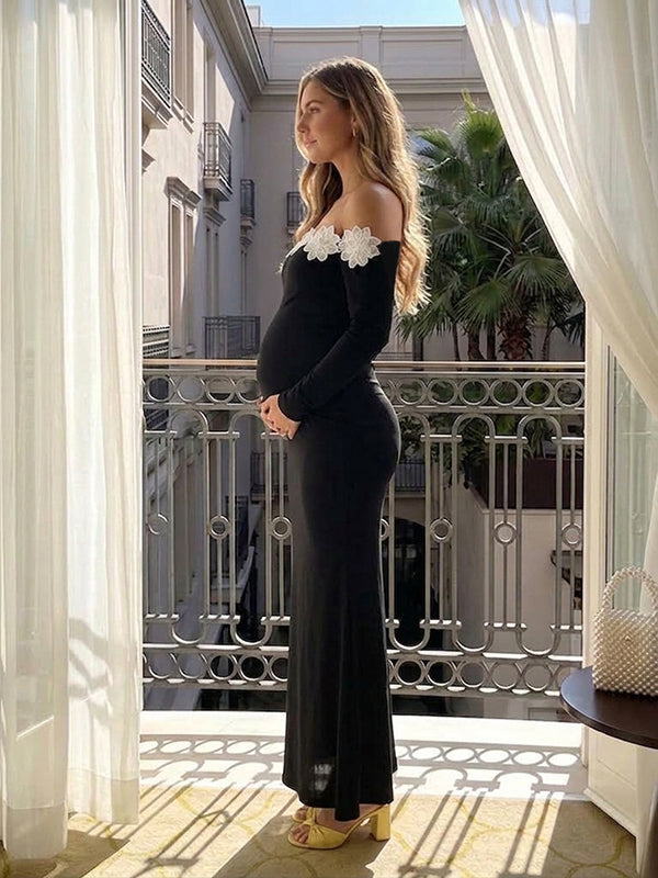 Side view of black off-shoulder maternity maxi dress with white 3D flower trim, long sleeves and mermaid hem, designed for baby shower and parties.