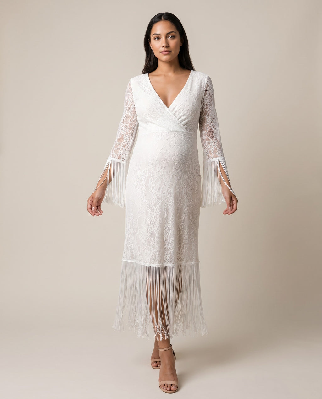 Ivory lace maternity maxi dress with deep V neckline and fringe trim on the sleeves and hem, shown on a pregnant model in studio.