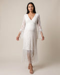 Ivory lace maternity maxi dress with deep V neckline and fringe trim on the sleeves and hem, shown on a pregnant model in studio.