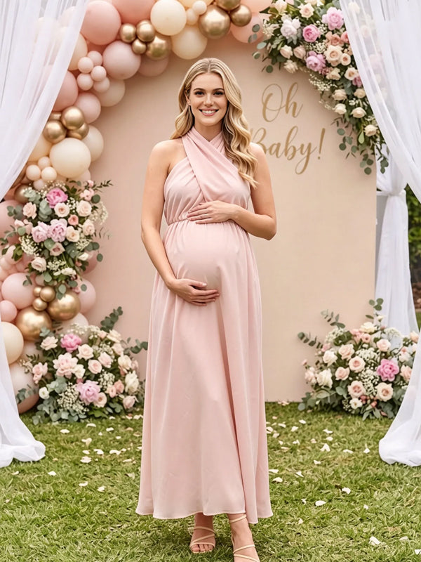 Pink flowy maternity maxi dress with crossover halter neck and tie back, designed for baby shower.