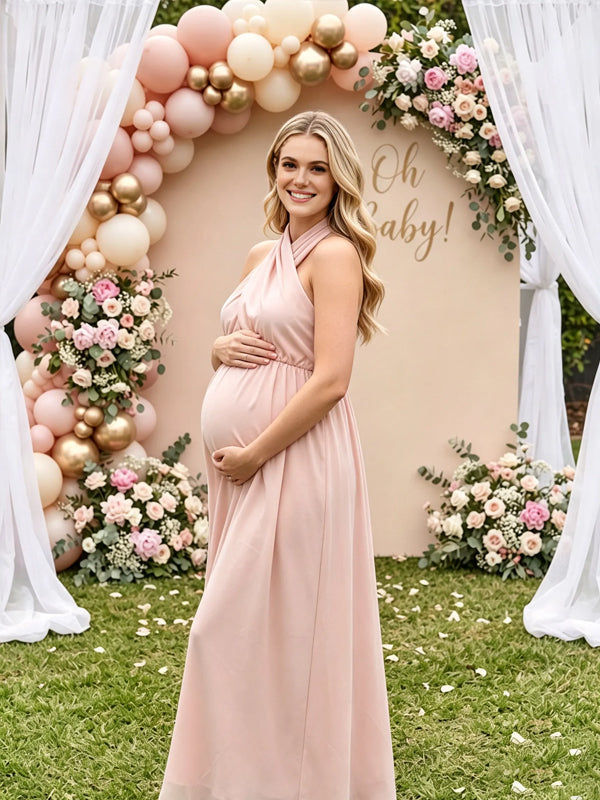 Pink flowy maternity maxi dress with crossover halter neck and tie back, designed for baby shower.