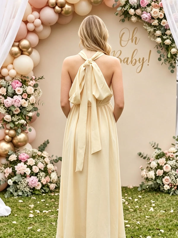 Back view of butter yellow flowy maternity maxi dress with crossover halter neck and tie back, designed for baby shower.