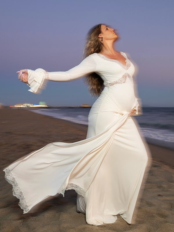 Ivory maternity maxi dress with lace-trimmed V-neck, ruffle bell cuffs, draped sash and mermaid train, designed for maternity photoshoot.