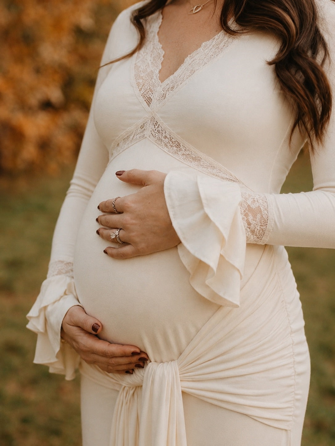 Ivory maternity maxi dress with lace-trimmed V-neck, ruffle bell cuffs, draped sash and mermaid train, designed for maternity photoshoot.