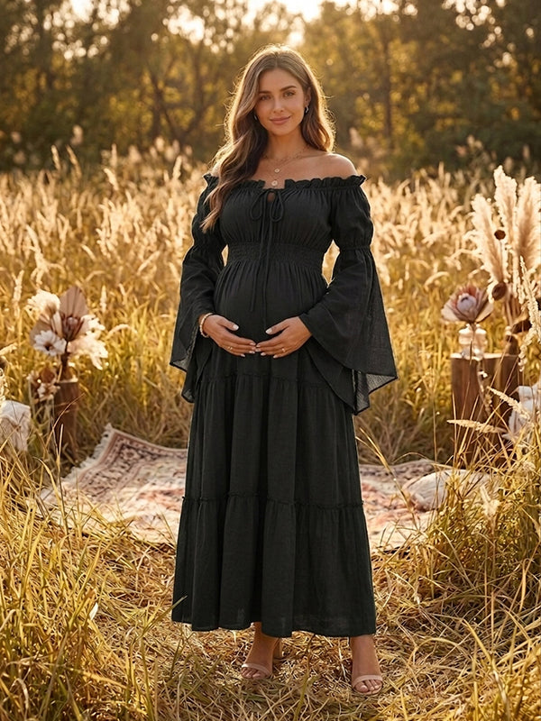 Black boho maternity maxi dress with off-shoulder smocked bodice, bell sleeves and tiered skirt, designed for maternity photoshoot.