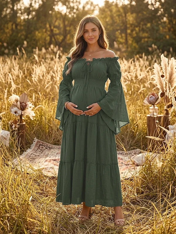 Forest green boho maternity maxi dress with off-shoulder smocked bodice, bell sleeves and tiered skirt, designed for maternity photoshoot.