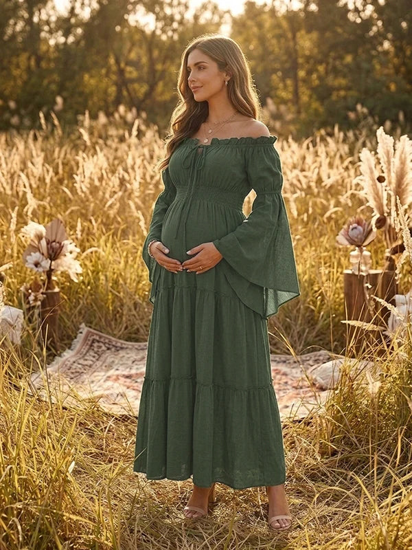 Forest green boho maternity maxi dress with off-shoulder smocked bodice, bell sleeves and tiered skirt, designed for maternity photoshoot.