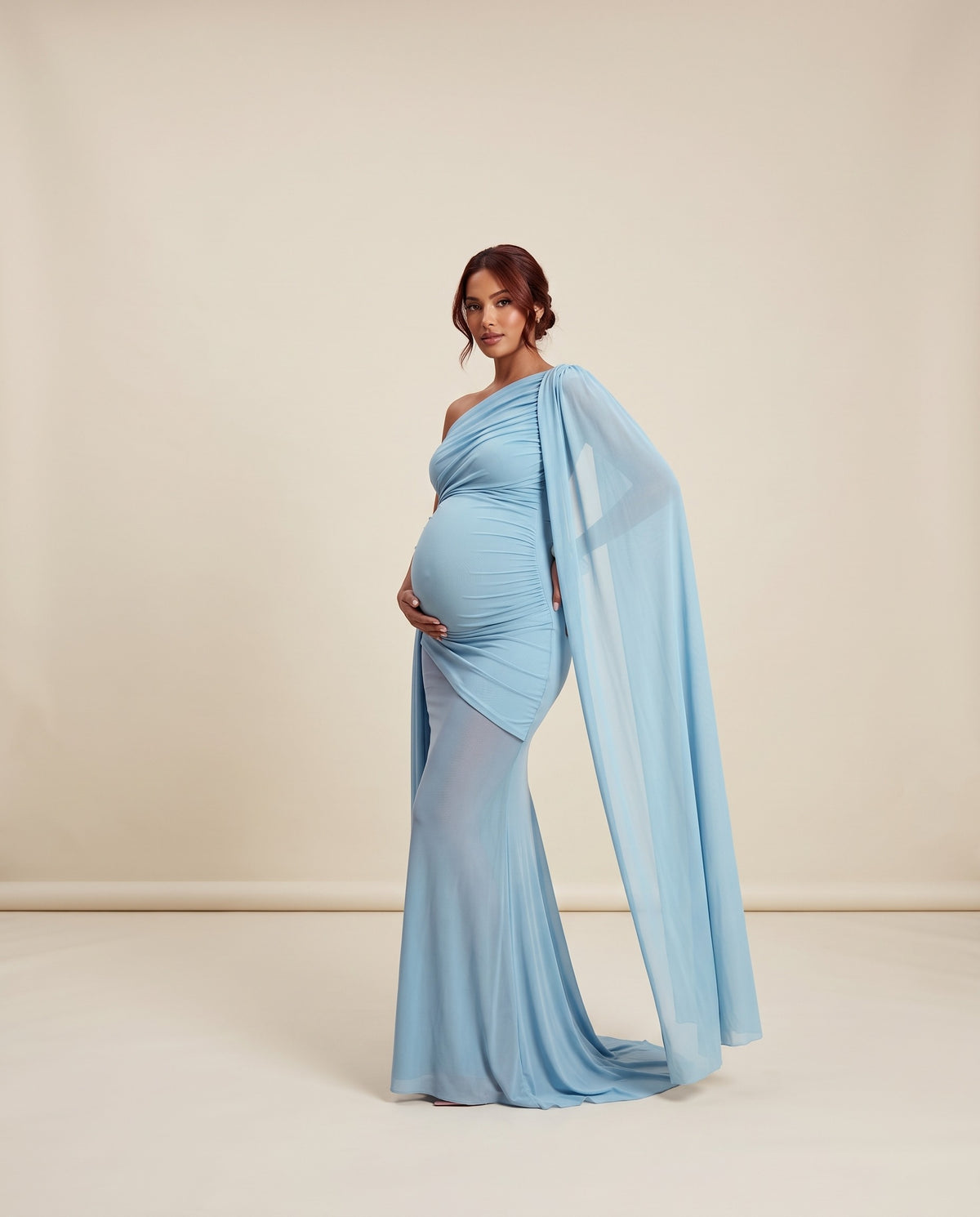 Blue mesh maternity maxi dress with one-shoulder neckline and flowing cape panel, designed for maternity photoshoots and formal events.