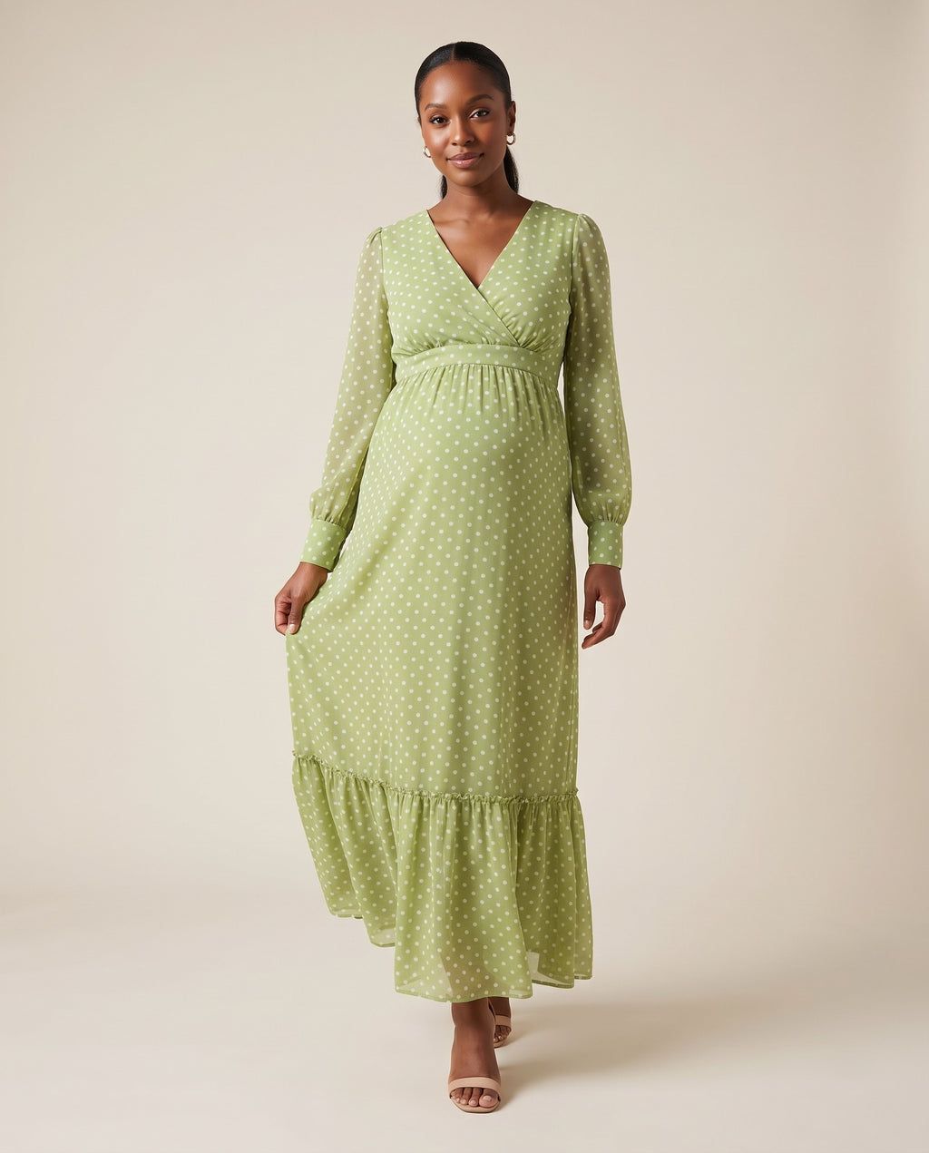 Green polka dot chiffon maternity maxi dress with wrap neckline and ruffle hem, shown on a pregnant model in studio.