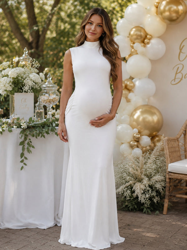White maternity maxi dress with mock neck, sleeveless bodice and side ruching, designed for baby shower.