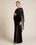 Black velvet maternity maxi dress with sheer floral lace cape panel and lace sleeves, shown on a pregnant model in studio.