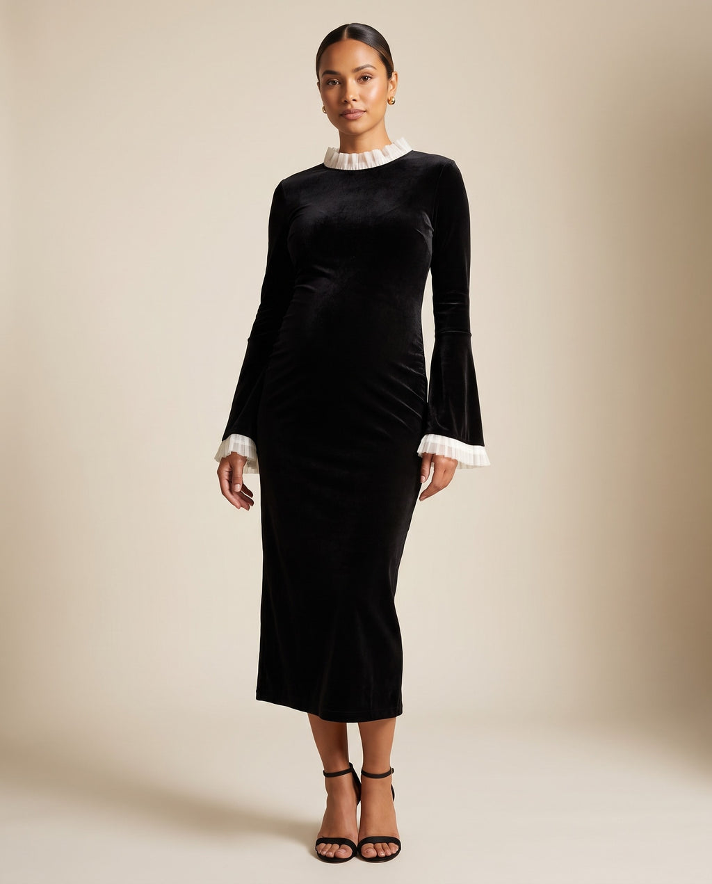 Black velvet maternity midi dress with ivory ruffle collar and cuffs, shown on a pregnant model in studio.